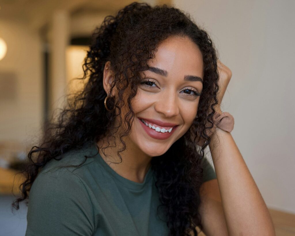 Woman with curly hair smiling warmly in a close-up portrait