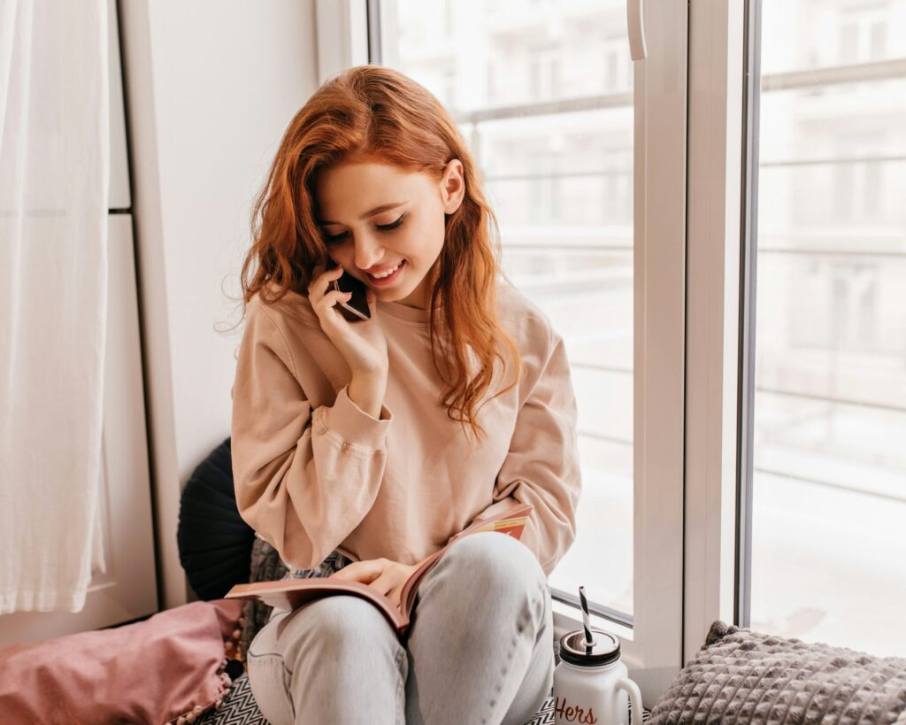 Woman smiling while talking on the phone beside a sunlit window