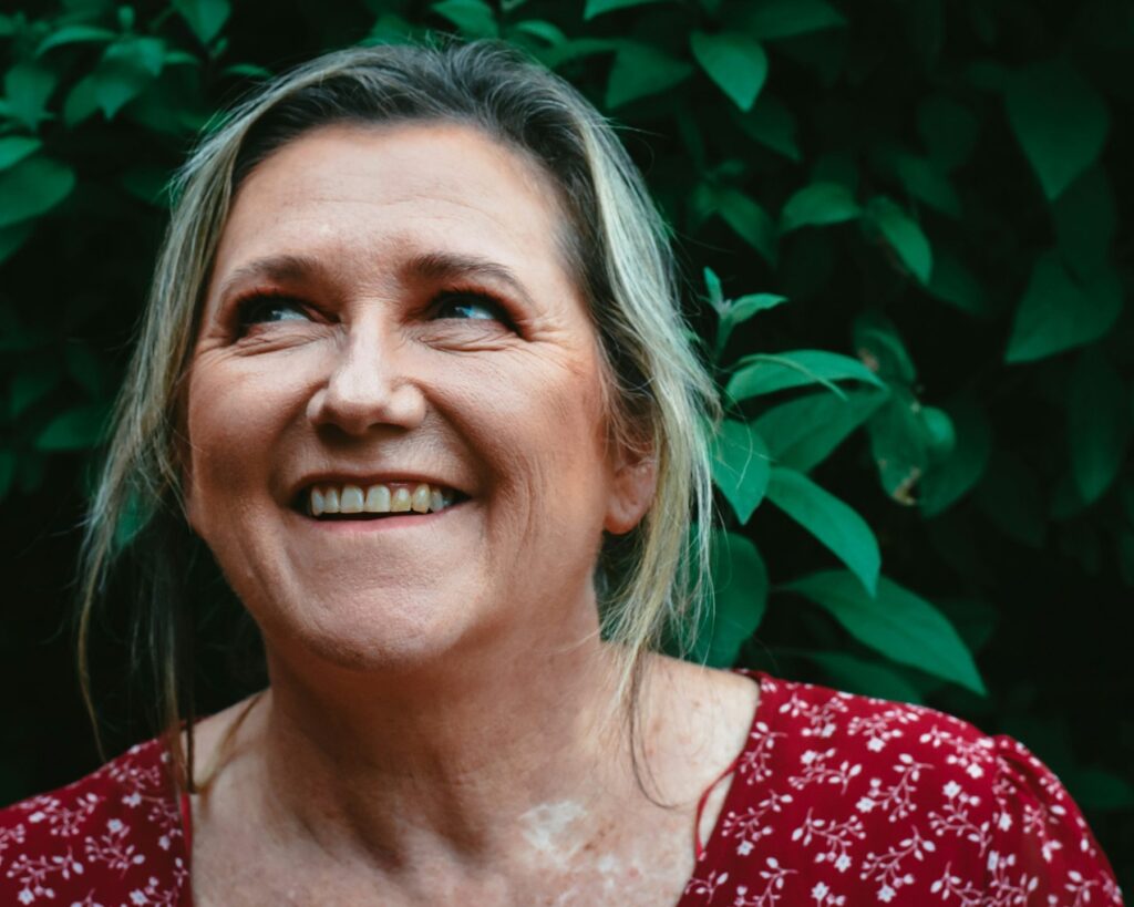 Woman in her 50s laughing warmly outdoors in front of green foliage