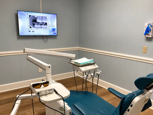 Treatment room with a blue patient chair and a wall monitor showing dental X-rays