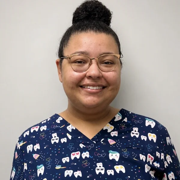 Monica Brown, front desk and treatment plan coordinator, smiling in navy dental scrubs